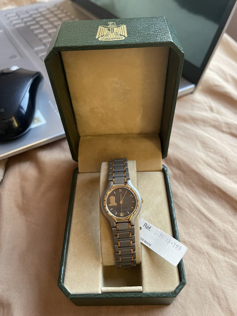 Green watch box with gold emblem open showing watch nestled in protective case
