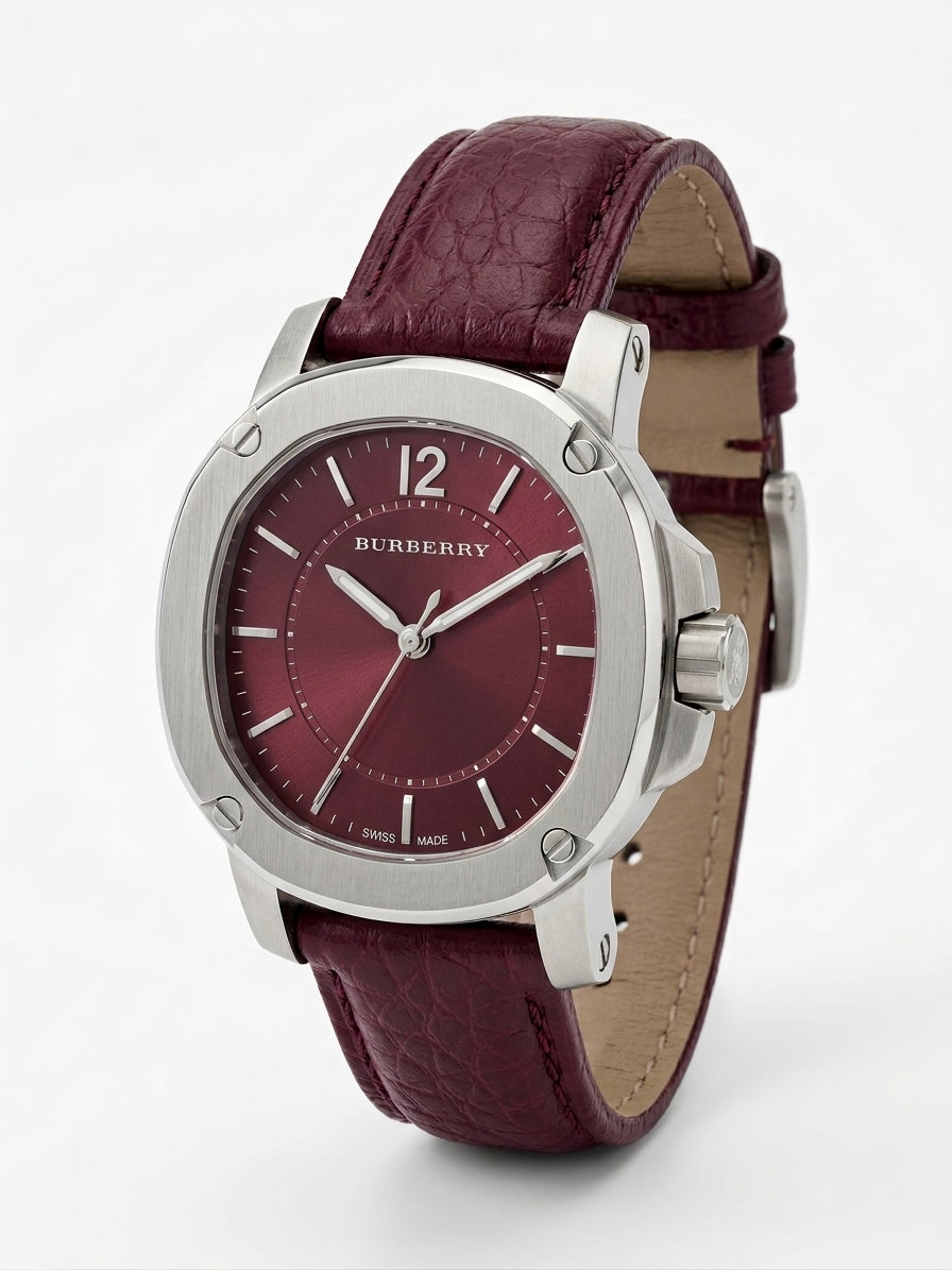 A Burberry men's watch featuring a silver-tone round case, a textured burgundy dial, and a matching burgundy leather strap with a tan interior lining, shown on a light gray background.